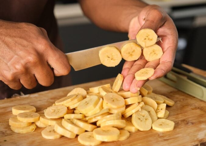 Photo shows a young African man's hands as he chops plantain in the kitchen
