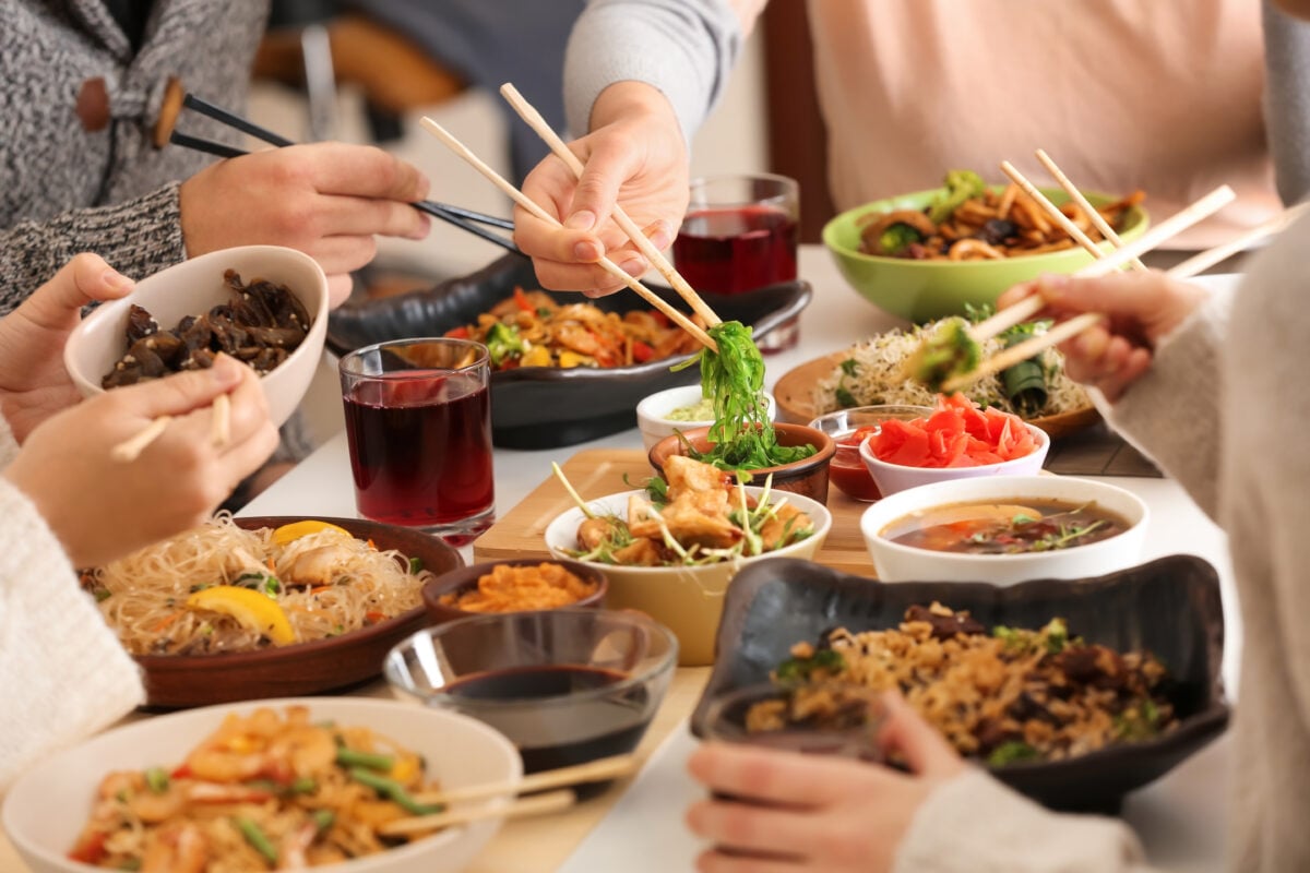 Photo shows a group of people sat at a table sharing bowls of food