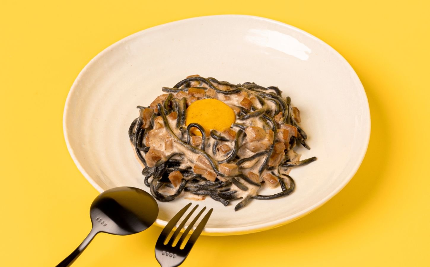 a bowl of charcoal spaghetti carbonara with vegan egg yolk and mushroom pancetta
