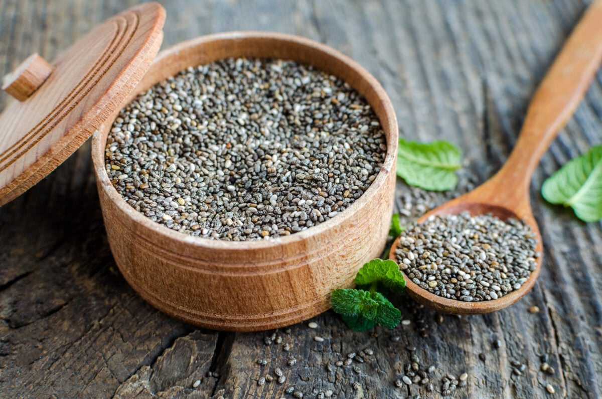 Photo shows chia seeds in a wooden bowl on old rustic wooden table with a matching wooden spoon