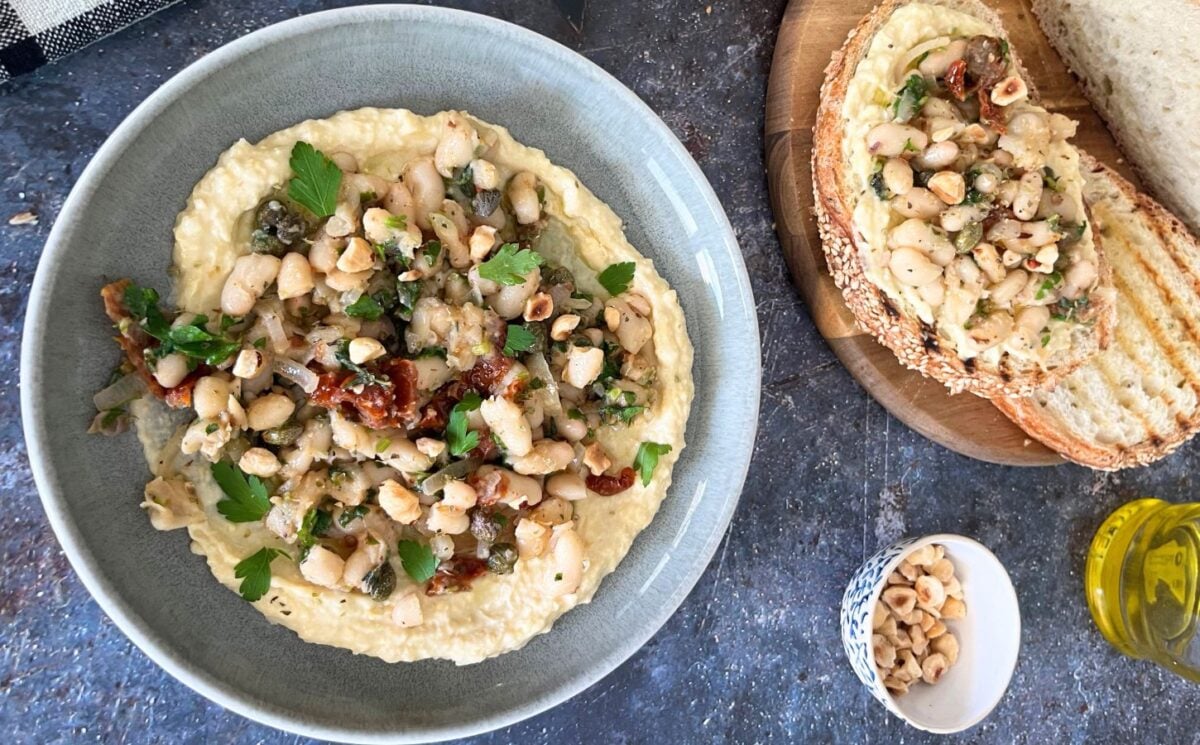 A bowl of Mediterranean beans on toast served with crusty bread and houmous