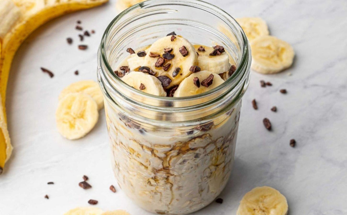 a glass jar full of vegan chocolate banana overnight oats topped with sliced banana and dark chocolate chips