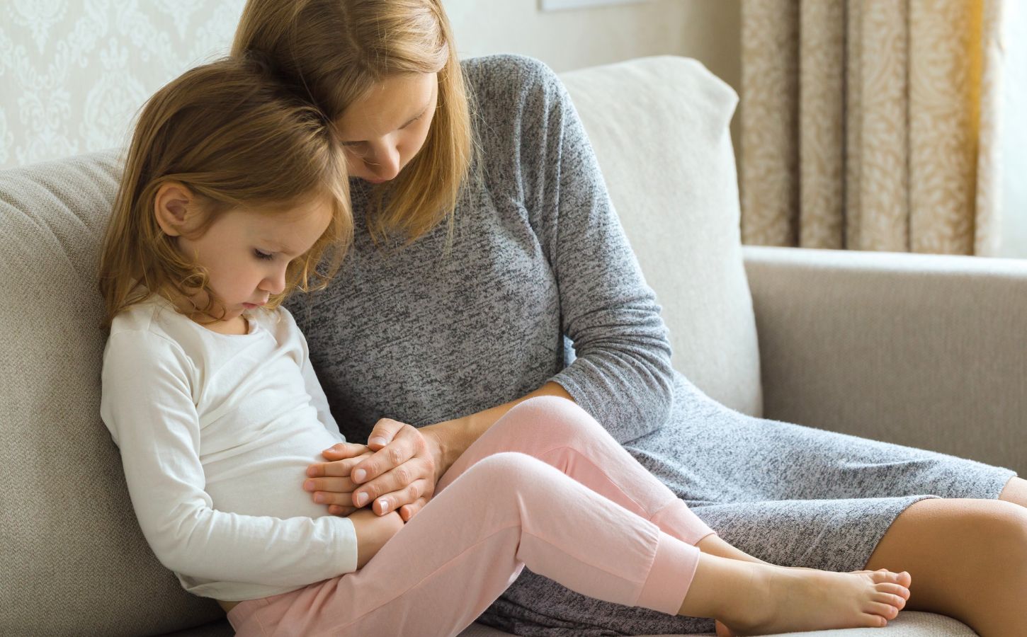 A child with digestive problems being consoled by her mother on the sofa