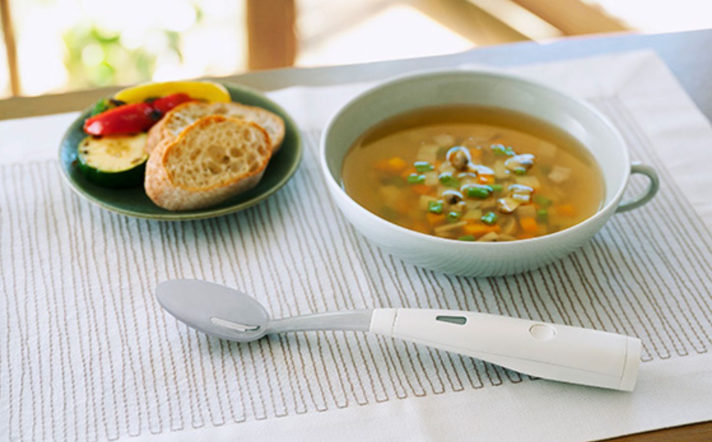 Photo shows the new Electric Salt Spoon next to a bowl of miso and a bread-based side on a white patterned table