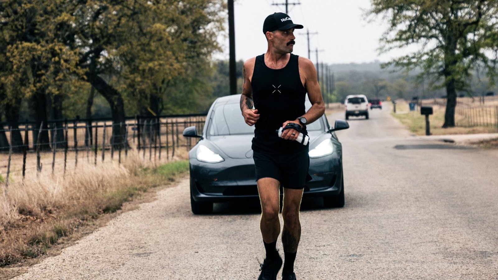 robbie balenger running in front of a tesla model 3 car