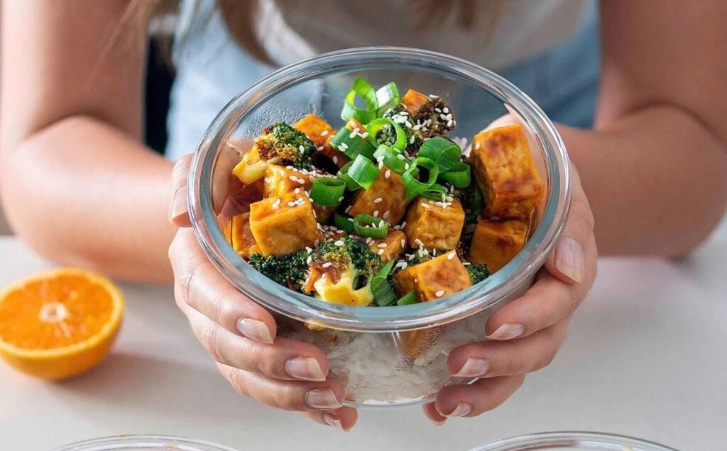 bowls of freshly prepared orange tofu and broccoli, one being held by the recipe developer from Plant Baes