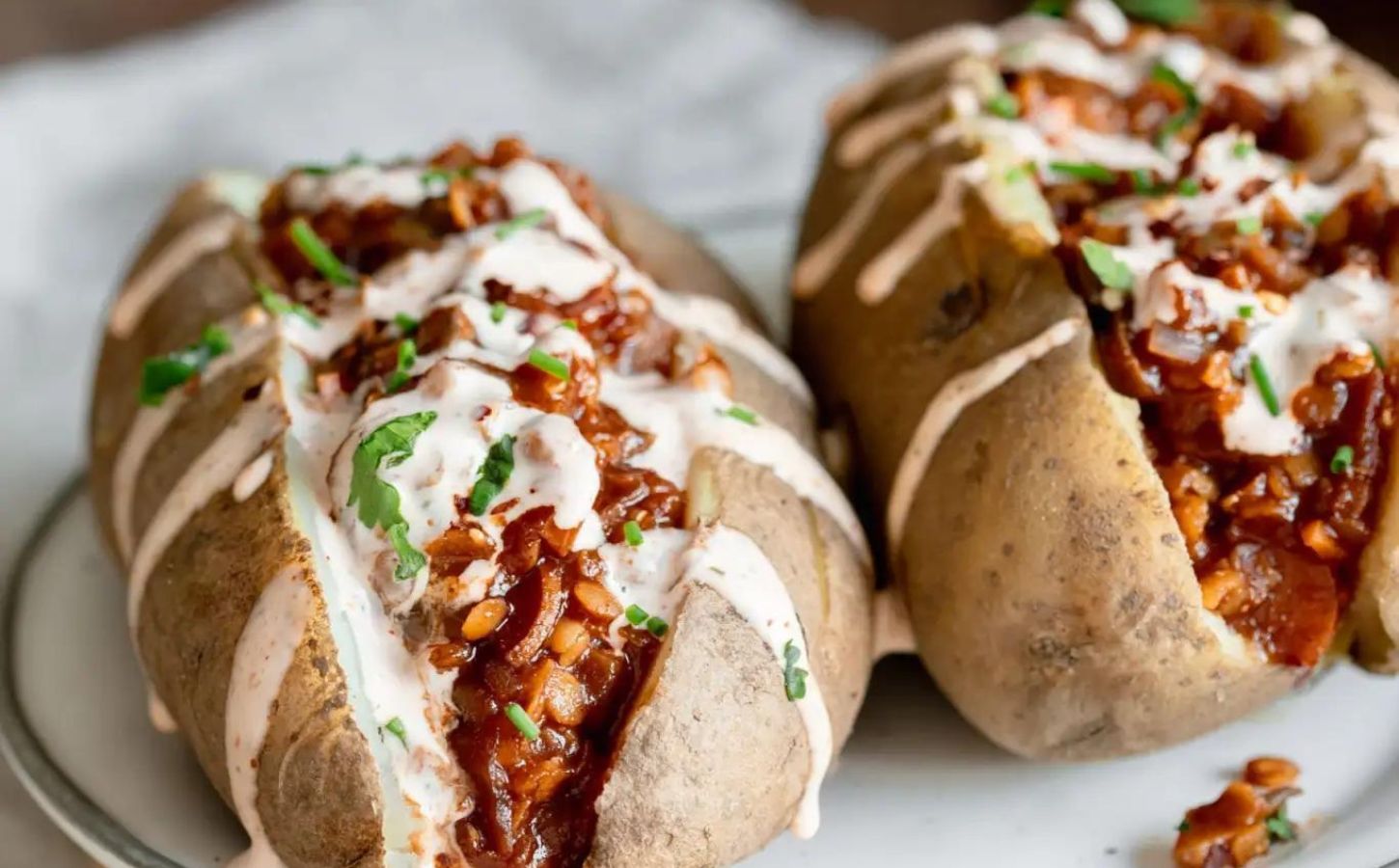 Two baked potatoes filled with smoky vegan barbecue lentils and drizzled with plant-based sriracha mayo