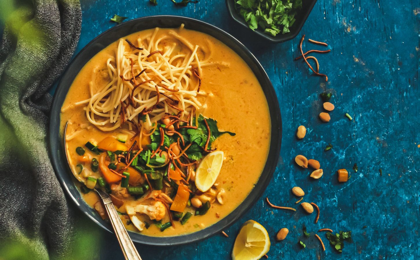 A black ceramic bowl filled with vegan khow suey soup recipe and topped with crunchy noodles and other garnishes