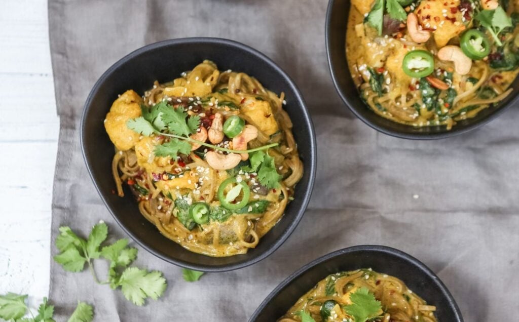 Three bowls of vegan spicy coconut noodles on a table