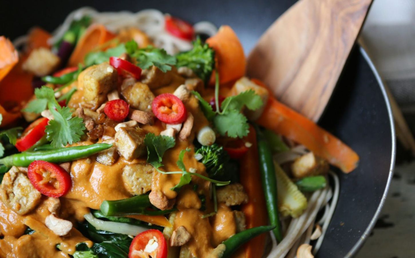 A close-up of a vegan stir fry featuring tahini, tofu, peppers, greens, carrots, and other veg