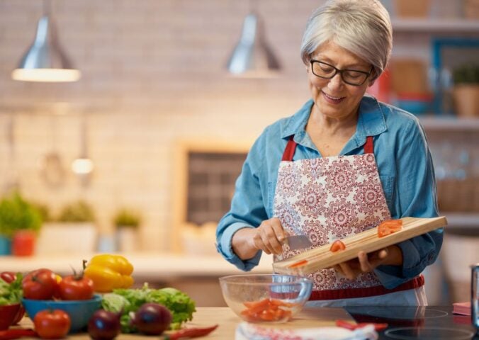 Photo shows a woman chopping vegetables in her kitchen