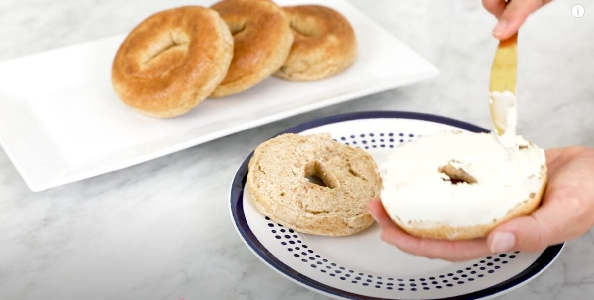 Whitney E. RD spreading cashew cream cheese on a vegan bagel, a food she eats during her plant-based pregnancy