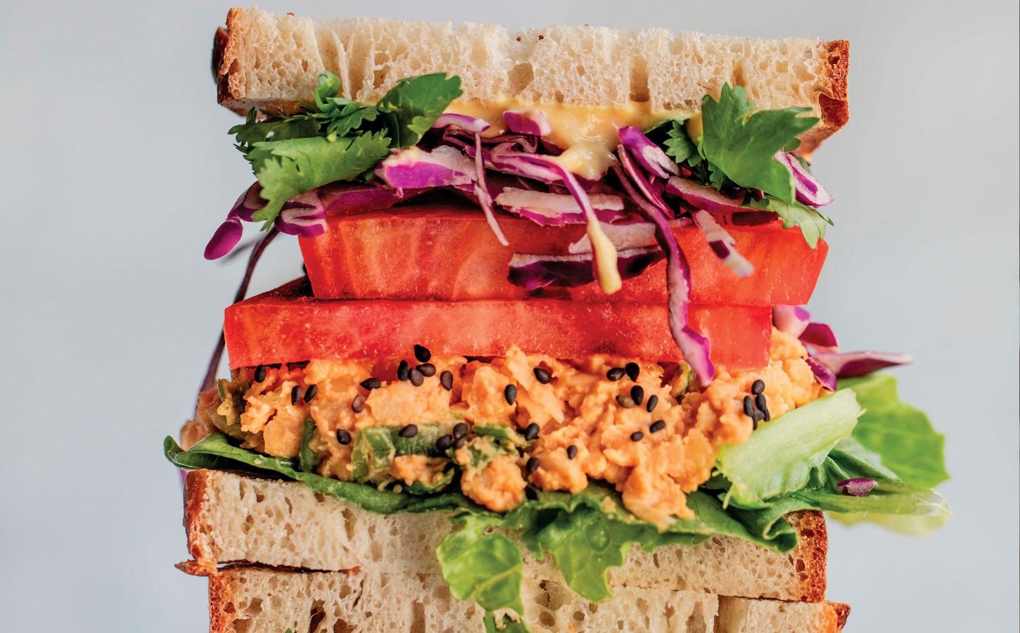 a picture of stacked peanut miso chickpea salad sandwiches with sesame, tomato, chickpea spread, and greens as part of vegan spring lunch ideas